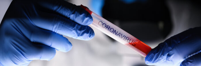 lab technician wearing gloves handles a test tube of blood that says coronavirus on it